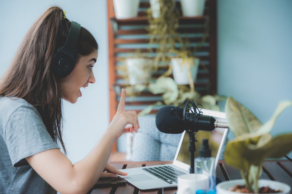 Young woman vlogger live streaming online with laptop and microphone